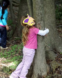 Girl hugging a tree with a butterfly eye mask on during Sheldrake birthday party.