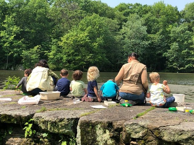 Kids sitting at Sheldrake pond's edge with naturalists during camp.