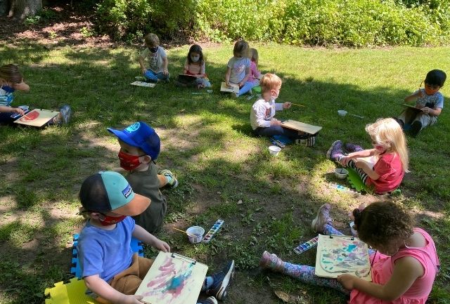 Kids sitting on Sheldrake lawn working on a painting project.