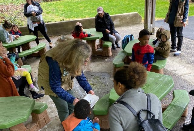 toddlers with their adult caregivers parents outdoors at tables making a nature craft