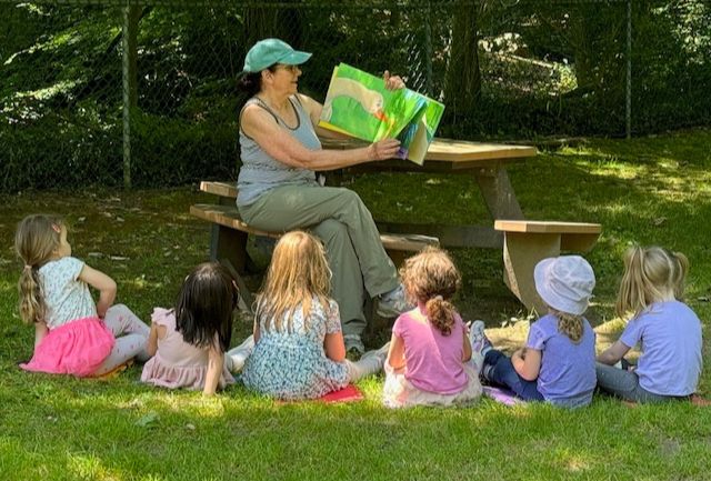 adult reading a story to a group of children sitting in the grass
