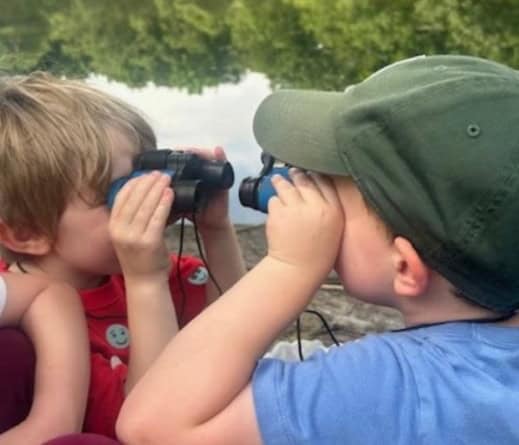 Two toddler boys looking at each other through binoculars.