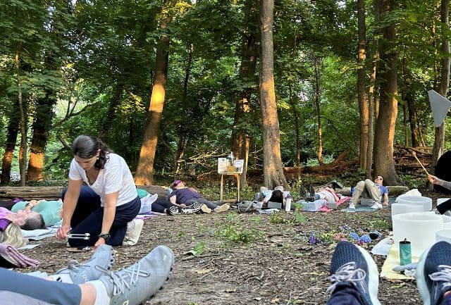 Group of adults lying on the ground on mats in a circle in the woods